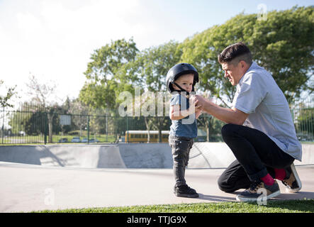 Vue latérale du père fils aidant dans le port de casque en skateboard park Banque D'Images