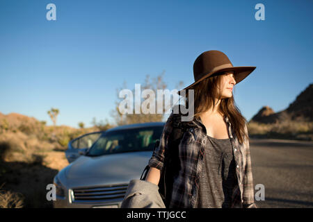 Femme au chapeau de soleil à l'écart en se tenant sur le route contre ciel clair Banque D'Images