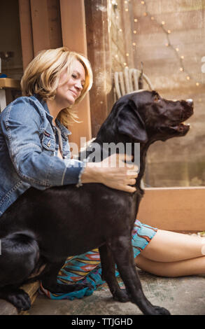 Happy woman looking at Black Labrador assis à la porte Banque D'Images