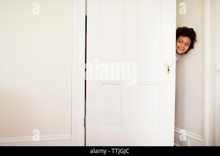 Happy boy peeking through door at home Banque D'Images