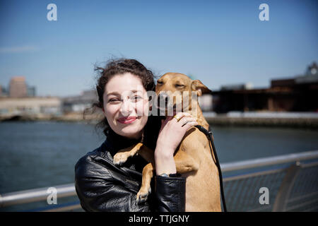 Portrait of happy woman with dog standing on footbridge against sky Banque D'Images