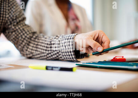 Portrait de main tenant un crayon alors que working in office Banque D'Images