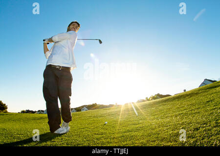 L'homme prenant une photo de golf en position debout contre un ciel clair Banque D'Images