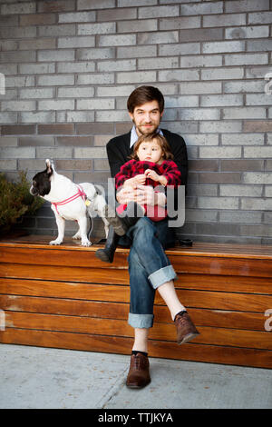 Portrait de l'homme assis avec sa fille sur un banc contre le mur Banque D'Images