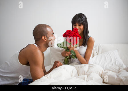 Man roses pour femme alors qu'assis sur le lit à la maison Banque D'Images