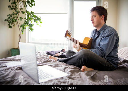 L'homme à l'aide d'un ordinateur portable pour l'apprentissage de la guitare à la maison Banque D'Images