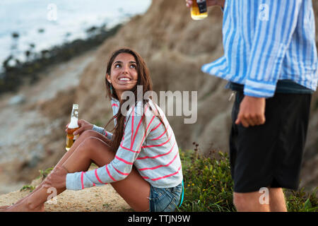 Femme avec bouteille de bière à la recherche au petit ami alors qu'il était assis sur terrain Banque D'Images