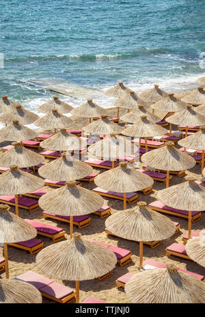 De nombreux parasols de paille de roseau avec chaises longues sur une belle plage de sable sur la côte Adriatique, une vue de dessus de l'antenne sur une journée ensoleillée sur la plage Banque D'Images