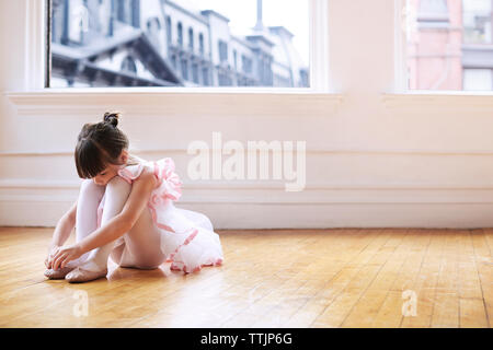 Girl wearing chaussures de ballet tout en restant assis sur le plancher de bois franc en studio Banque D'Images