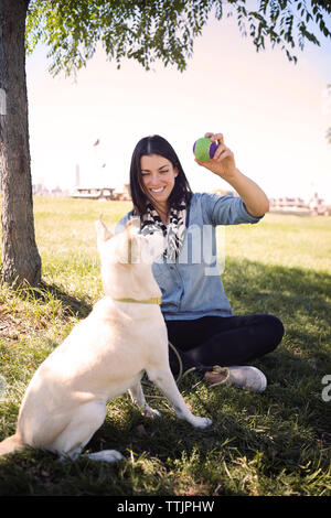 Happy woman showing balle pour chien ludique au parc contre le ciel Banque D'Images