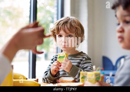 Les garçons de boire des jus de fruits à table durant le repas en maternelle Banque D'Images