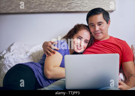 Loving couple looking at laptop computer while lying on bed at home Banque D'Images