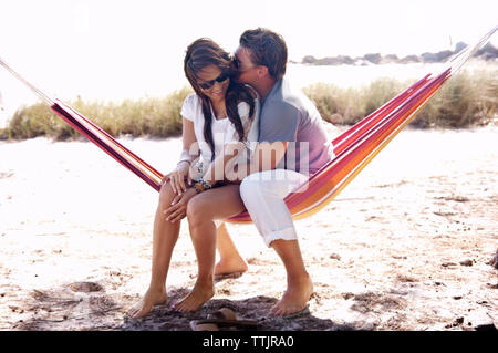 Affectionate couple sitting in hammock on field Banque D'Images