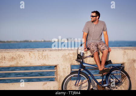 L'homme souriant à l'écart tout en étant assis sur un mur contre la mer Banque D'Images