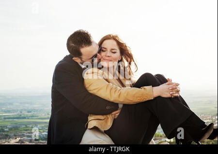 Man kissing woman tout en restant assis sur mur de retenue contre le ciel Banque D'Images