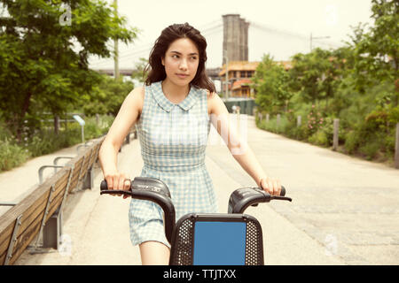 Woman riding bicycle on street contre Pont de Brooklyn en ville Banque D'Images