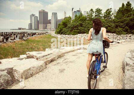 Vue arrière du vélo avec femme debout sur voie par rivière en ville Banque D'Images