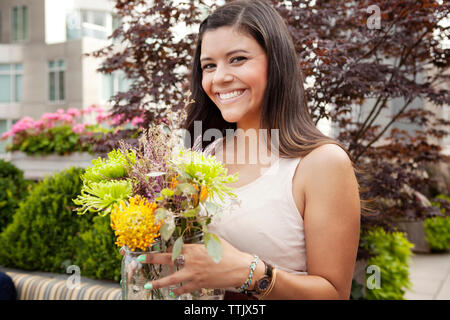 Smiling woman holding Flowers pot debout contre des plantes Banque D'Images