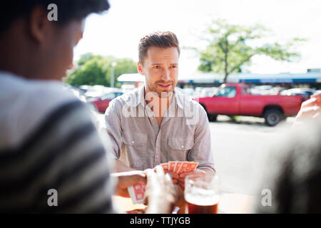 Man ami tout en jouant aux cartes dans la fenêtre table contre brewery Banque D'Images