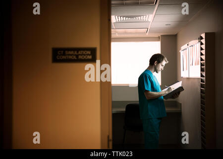 Lecture des rapports tout médecin standing in hospital ward Banque D'Images