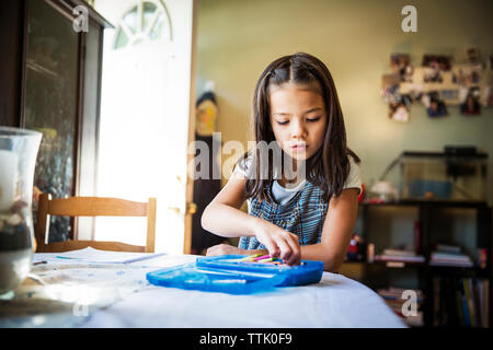La prise de crayon fille fort tout en étant assis à table Banque D'Images