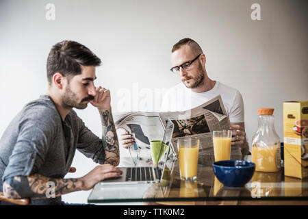 Gay man reading newspaper partner à table de petit déjeuner Banque D'Images