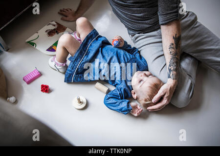 Portrait du père assis par daughter lying on floor at home Banque D'Images