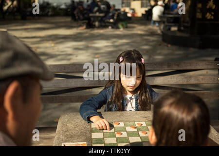 Jeune fille à la recherche vers le bas tout en jouant le jeu de dames avec sœur dans park Banque D'Images