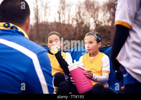 Joueurs de football à l'écoute de l'eau potable tandis que l'entraîneur au cours de match Banque D'Images