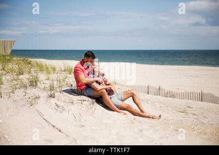Couple homosexuel se reposant sur la plage contre le ciel Banque D'Images