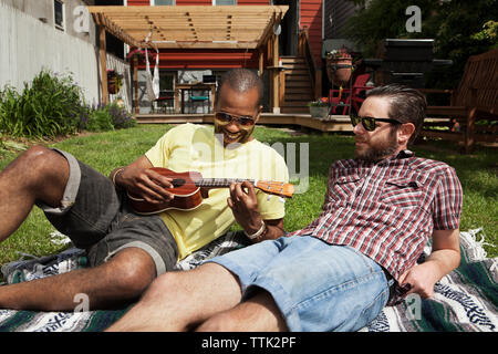 Amis jouant ukulele tout en vous relaxant sur terrain en pelouse Banque D'Images