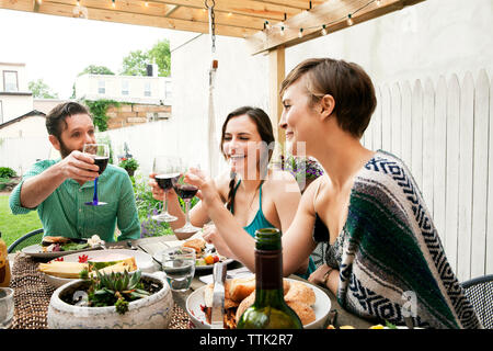 Friends toasting wineglasses while sitting at table in yard Banque D'Images