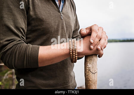 Portrait man holding baguette de bois debout par lake Banque D'Images