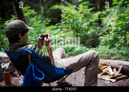 Randonneur à l'aide de smart phone alors qu'elle repose sur le fauteuil à camp site Banque D'Images