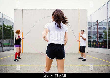 Femme marche vers friends holding jump ropes on street contre mur Banque D'Images