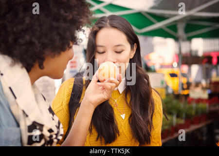 Woman smelling fruit tenu par ami at market Banque D'Images