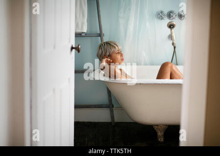 Thoughtful woman relaxing in bathtub at home Banque D'Images