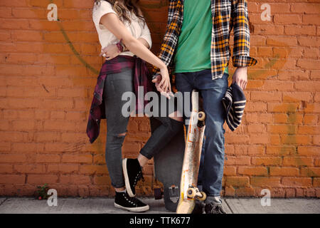 La section basse du couple holding hands while standing against brick wall Banque D'Images