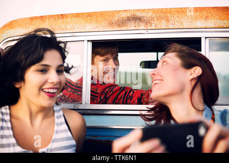 Cheerful woman à l'aide de téléphone portable en voyage avec des amis Banque D'Images