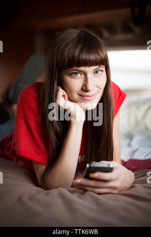 Portrait of young woman smiling while relaxing on bed in camper van Banque D'Images