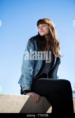 Woman smiling while sitting on mur de retenue contre ciel clair-- Banque D'Images