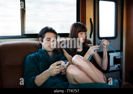 L'homme à l'aide de téléphone portable en tricot femme sur canapé dans le camping-car Banque D'Images