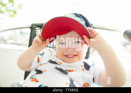 Close-up portrait of cute baby boy wearing cap tout en restant assis sur une chaise contre le ciel clair à la cour Banque D'Images