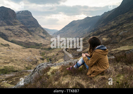 Vue latérale du woman sitting on mountain against sky Banque D'Images