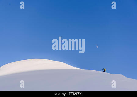 Woman climbing up snowy mountain avec lune en haut Banque D'Images