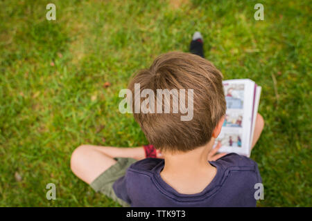 Portrait of boy reading comic book while sitting on grassy field at park Banque D'Images