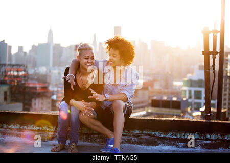 Heureux couple enjoying sur toit contre le ciel au coucher du soleil Banque D'Images