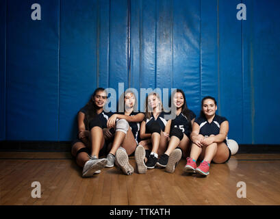 Portrait de filles assis sur un plancher en bois contre le mur bleu Banque D'Images