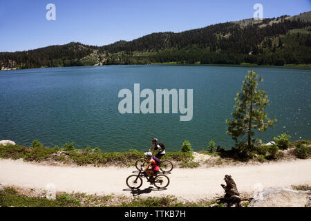High angle view of cyclists riding bicycles on dirt road by lake Banque D'Images
