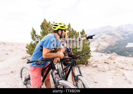 Couple avec des bicyclettes à la route en position debout contre la montagne ciel nuageux Banque D'Images